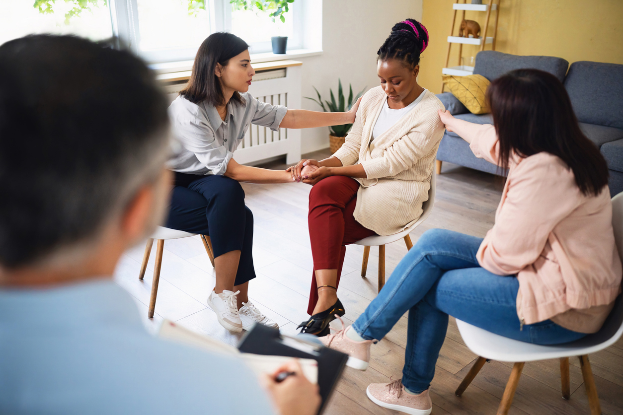 Women consoling a sad woman of Black ethnicity after she shared her thoughts and emotions during group therapy.